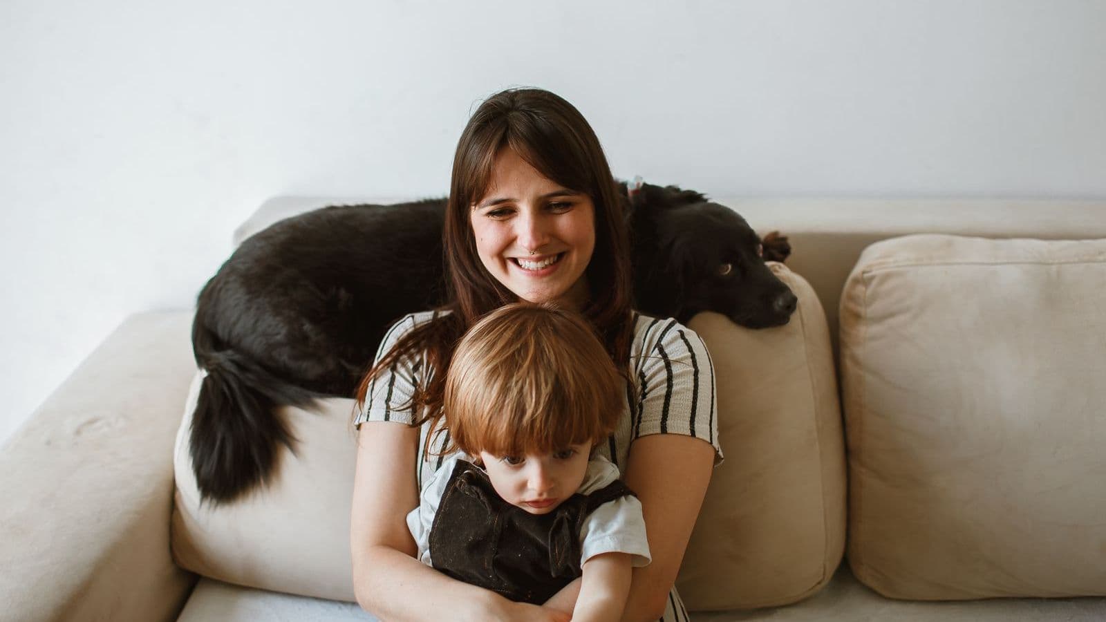 A woman with a dog and a toddler on a sofa