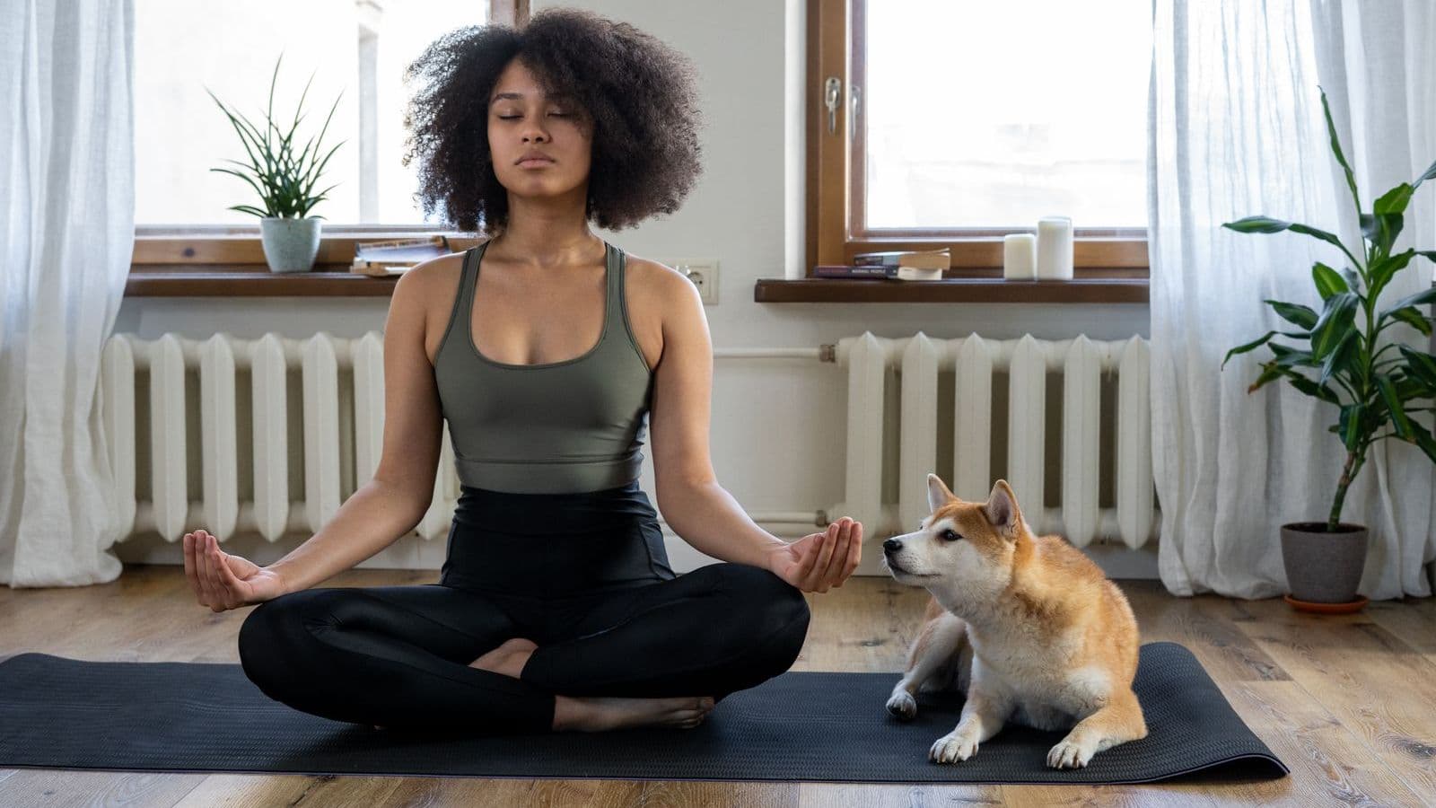 A woman on a yoga mat with a Shiba Inu settled beside her